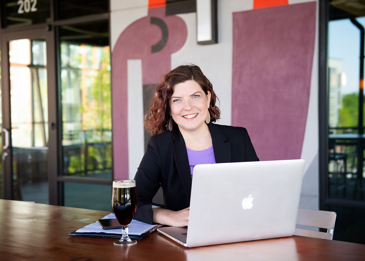 A woman working on her laptop with a dark beer and notepad