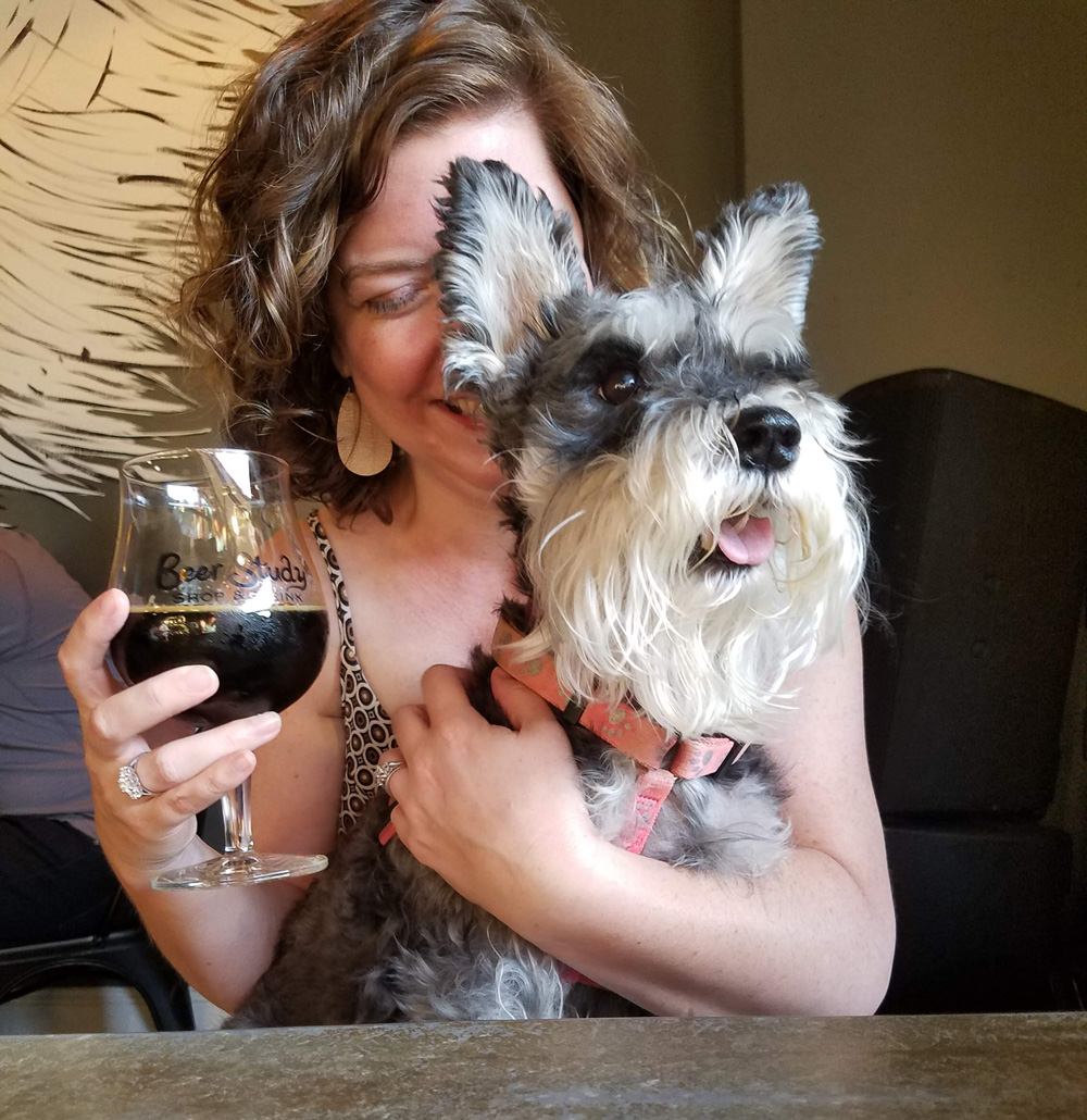 a woman smiling with dog and dark beer